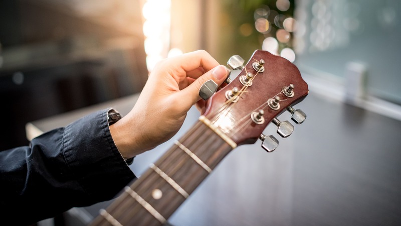 Accordare la chitarra, mano maschile che sta accordando la chitarra